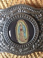 Close-up of the front showing the ornate embossed pewter design and the Virgin Saint image under a clear window.