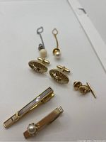 Image showing gold and silver plated cuff links with pearl decorations and mother of pearl inlay tie clips on white background.