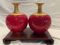 Front view of the pair of red porcelain vases with gold glaze on the neck, placed on a wooden base