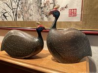 Pair of hand-carved crowned guineafowl bird sculptures side by side on wooden surface, showing full body.