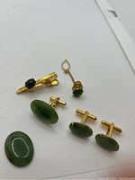 Set of two pairs of green jade cuff links and two tie clips on white surface, showing overall items and their details.