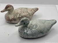 Front and angled view of two ceramic duck figurines showing marbled brown and green finishes with glossy surfaces.