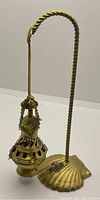 Side view of the vintage brass incense burner hanging from the twisted brass stand with a shell base and a painted gold crusader cross on the base