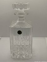 Front view of the square vintage crystal decanter showing the cut crystal design and stopper with a gold sticker.