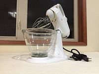 Full side view of white KitchenAid Model C3 stand mixer with attached glass mixing bowl and paddle/whisk mixer attachment. Plugged in power cord visible.