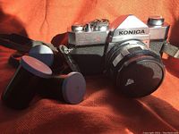 Photo of the vintage Konica Autoreflex A 35mm SLR film camera with lens caps on an orange background and three vintage film rolls next to it.