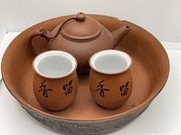 Yixing clay teapot, two cups inside a large round tray, showing the brown ceramic with Chinese characters on cups.