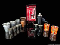 Full collection of vintage barware and travel sets displayed on a black reflective surface with all items visible