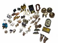 Top-down view of the entire vintage jewelry collection spread out on a white background showing various earrings, pins, and brooches with a copper link bracelet.