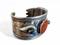 Angled view of silver cuff bracelet showing large oval orange carnelian stone bezel set, small teardrop lapis lazuli stone, and gold inlay tribal design with silver beaded borders.