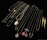 Multiple gold-tone necklaces and a pair of gold-tone tassel earrings spread on black background, showing different pendant designs and chain styles.