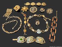 Photo showing all vintage gold-tone costume jewelry items including bracelets, brooches, necklaces, and a large ring arranged and displayed on a black background for clear visibility of details and colors.