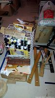 Wide view of drafting rulers, paint bottles in wire carrier, brushes, and wooden patterns on floor.