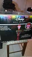 Box of the Disney Magic Holiday Mickey Mouse Light Ribbons LED Projection Light Post showing colorful packaging and product images.