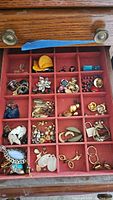 Wood drawer with multiple compartments filled with assorted earrings and pendants in various styles, sizes, and colors.