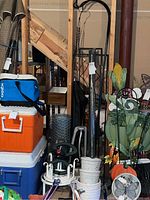 Wide view showing lot contents including coolers, ceramic planters, black metal planter stands, metal chicken wire roll, garden decorative items, and black metal trellis and shepherd's hook.