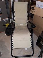 Full view of beige canvas lounger in reclined position showing black metal frame and attached back support pillow.