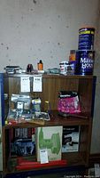 Wide view of wooden shelving containing various hardware and tool items including glue, adhesive cans, small packaged hardware parts, and boxed items.