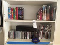 Shelf with VHS tapes including Planet of the Apes series, a variety of DVD and CD cases, and a black VHS cassette case.