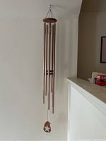 Full view of wind chime showing six bronze metal tubes hanging from a wooden round top, with wooden wind catcher at bottom with star cutout.