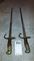 Pair of WWII bayonet swords with rusted blades and wooden handles with brass fittings