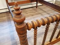 Close-up of wooden turned finial and spool spindle detailing on the bed's footboard post.