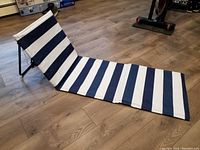 Folding beach chair mat laid out flat showing navy and white horizontal stripes and angled backrest on wooden floor