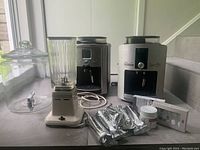 Full view of 2 espresso machines, vintage blender, glass jar, and coffee accessories on table