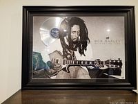 Front view of framed Bob Marley poster with mounted silver vinyl record showing full artwork and frame.