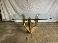 Full view of brass dolphin coffee table with glass top on concrete floor