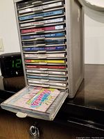 Metal CD rack with multiple slots filled with CDs, one slot pulled out showing colorful CD cover for 'Polka Polka Polka'