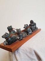 Side view of soapstone sled dog team with musher on wooden base showing five dogs with leather harnesses.