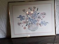 Frontal view of the framed floral picture with light-colored flowers in a glass vase, showing the frame and matting.