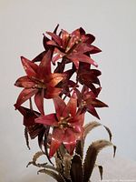 Handcrafted metal sculpture of red flowers with golden stamens and textured greenish-gold leaves on a base seen from front.