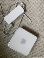 Photo of Apple Mac Mini unit with power adapter and attached cable on carpeted floor.