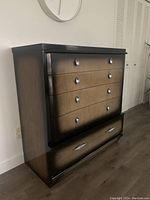 High boy dresser showing dark frame, light wood drawer fronts with silver metal pulls.