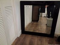 Square mirror leaning against a wall showing reflective surface and black lacquer frame.