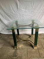 Full view of square side table with clear beveled glass top and metal base with gold and dark green accents