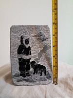 Front view of soapstone carving showing Inuit figure and bear with measurement tape beside for scale.