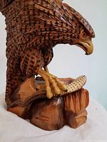 Close-up view of the larger bird sculpture showing detailed carved feathers, hooked beak, and talons gripping a wooden rock base.
