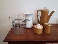 Photo showing all vessels together on wooden surface: Pyrex glass carafe, MCM coffee pot, creamer, sugar bowl, handcrafted vase