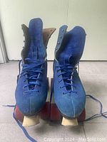 Front view of vintage blue suede roller skates size 8.5 with laces tied, showing toe stops and boot shape.