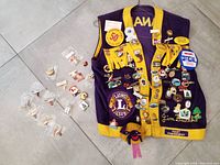 Purple and yellow Lions Club vest with numerous pins and patches on front, including Lions Club logos and pins from various events and locations.
