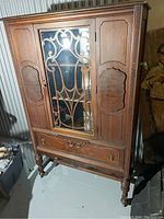 Front view of the antique china cabinet showing central glass door with metal grille and wooden side doors.