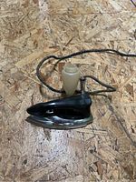 Photo of antique electric steam iron on wooden surface showing side profile with attached cloth-covered cord and steam knob.