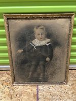 Full front view of the antique hand-tinted photographic portrait of a child, showing the image and the ornate decorative frame with visible wear and some damage.