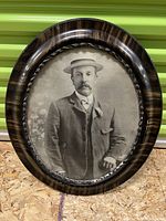 Frontal view of the antique oval wooden framed black and white photographic portrait of a man in vintage attire including a boater hat and suit.