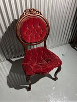 Wooden Victorian style chair with a round backrest, floral carved wooden frame, and red velvet tufted fabric upholstery with visible wear and distress