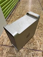 Silver aluminum Apple Mac Pro tower showing side and top with handle, minor scratches and dust visible.