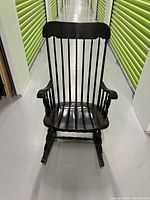 Front view of black vintage rocking chair showing spindle back, armrests, contoured seat, and curved rockers.